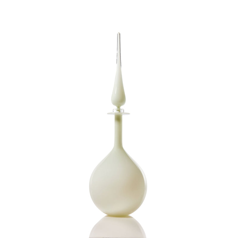 The Petite Tear Drop Decanter, in ivory, features a translucent pear-shaped glass body with a slender pointed stopper, standing upright on a reflective white surface against a plain white background.