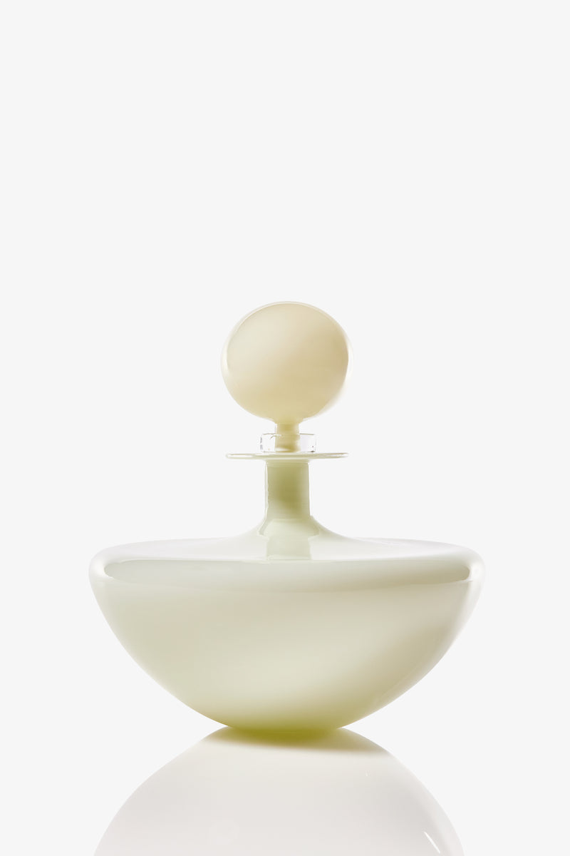 The Petite Low Arc Decanter features a modern, minimalist design with a rounded base and spherical cap in glossy, opaque white glass, displayed against a white background with a soft reflection below.