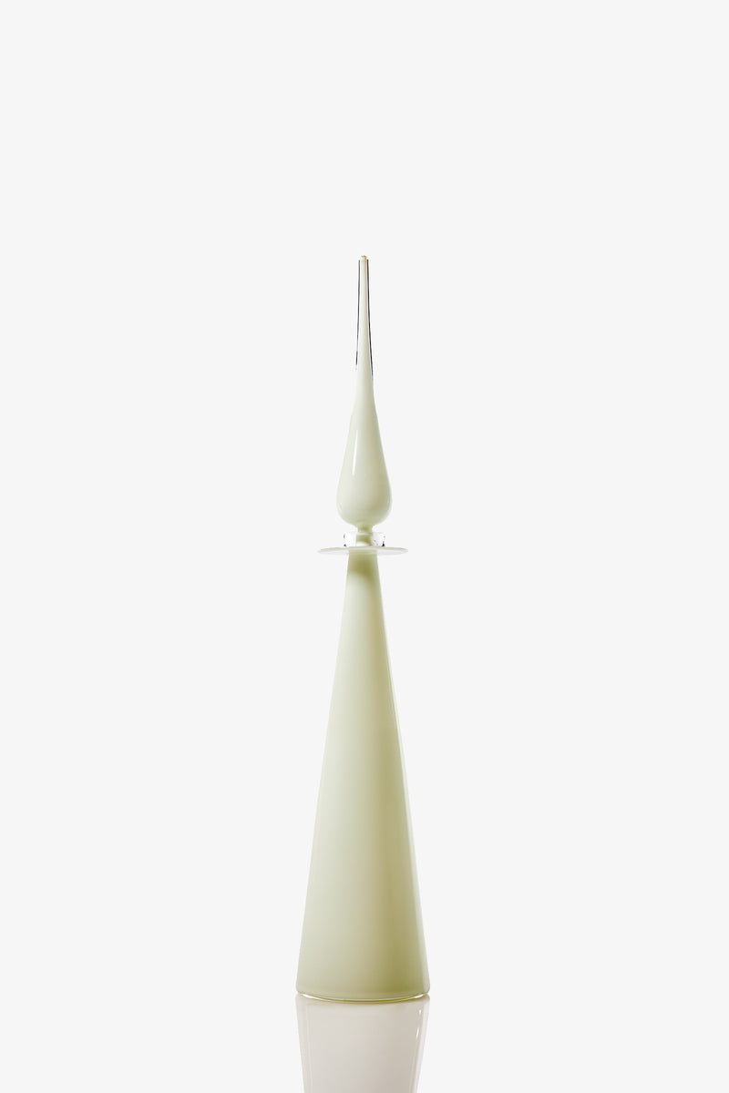 The Petite Straight Cone Decanter is a tall, slender, glossy pale green glass bottle with a pointed, elongated stopper on top, displayed against a plain white background.