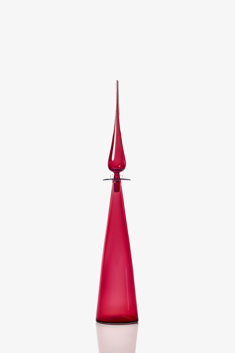 The Petite Straight Cone Decanter is a tall, elegant deep red glass bottle featuring a narrow base, pointed stopper, and reflective surface, showcased against a plain white background.