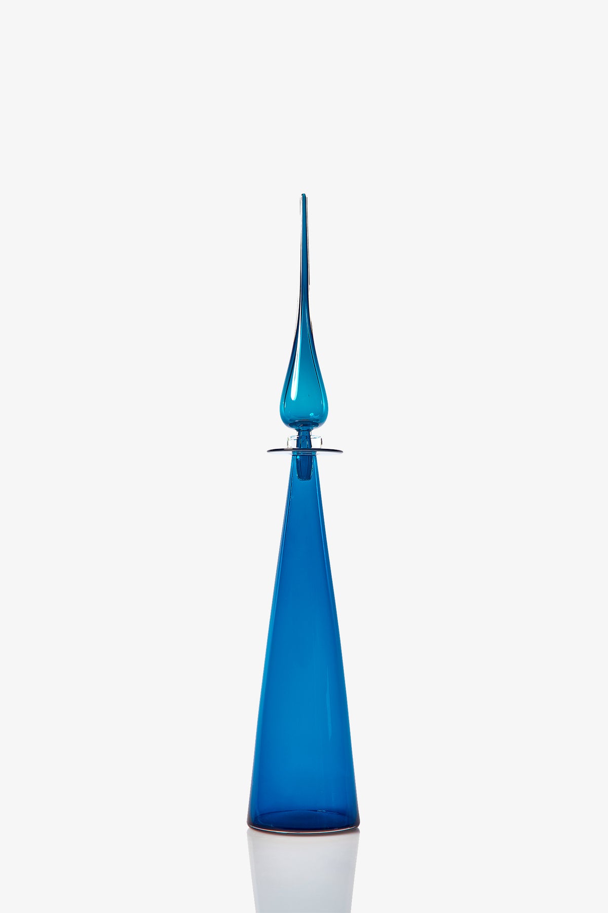 The Petite Straight Cone Decanter is a tall, sleek blue glass bottle with a pointed stopper and a modern, elongated conical shape, shown against a plain white background.