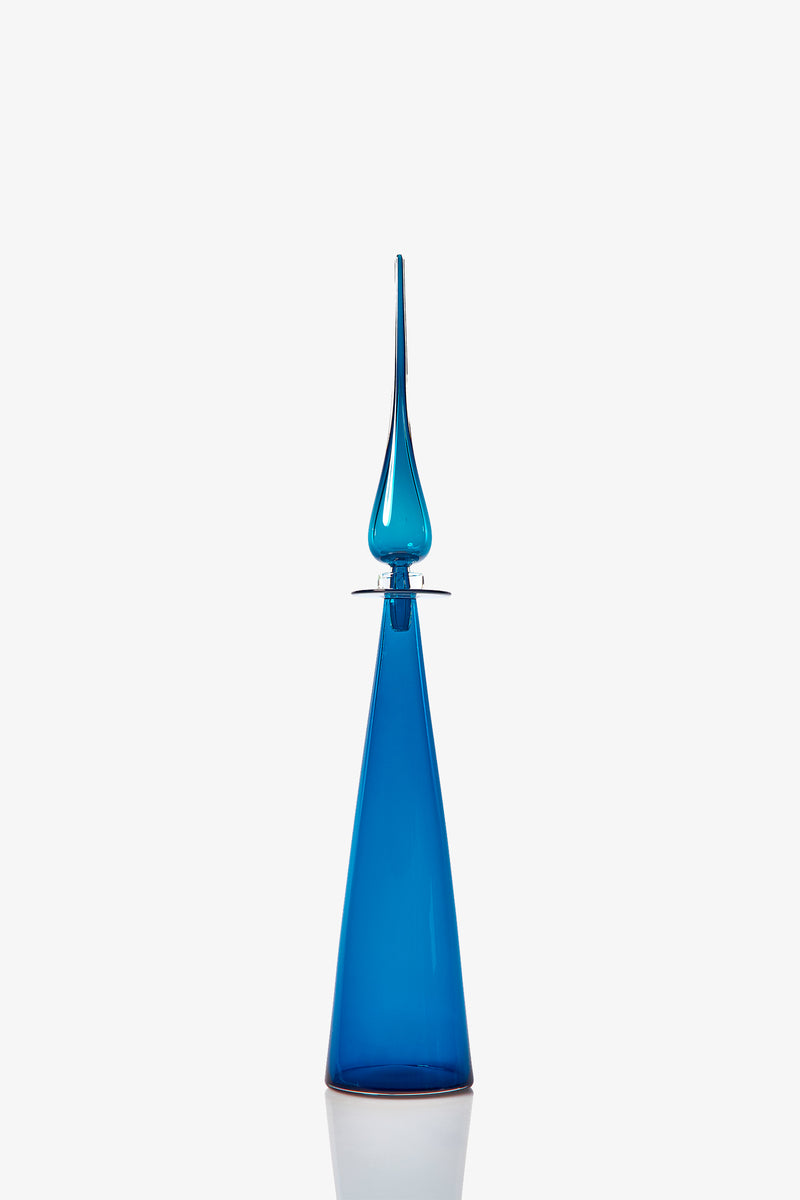 The Petite Straight Cone Decanter is a tall, sleek blue glass bottle with a pointed stopper and a modern, elongated conical shape, shown against a plain white background.