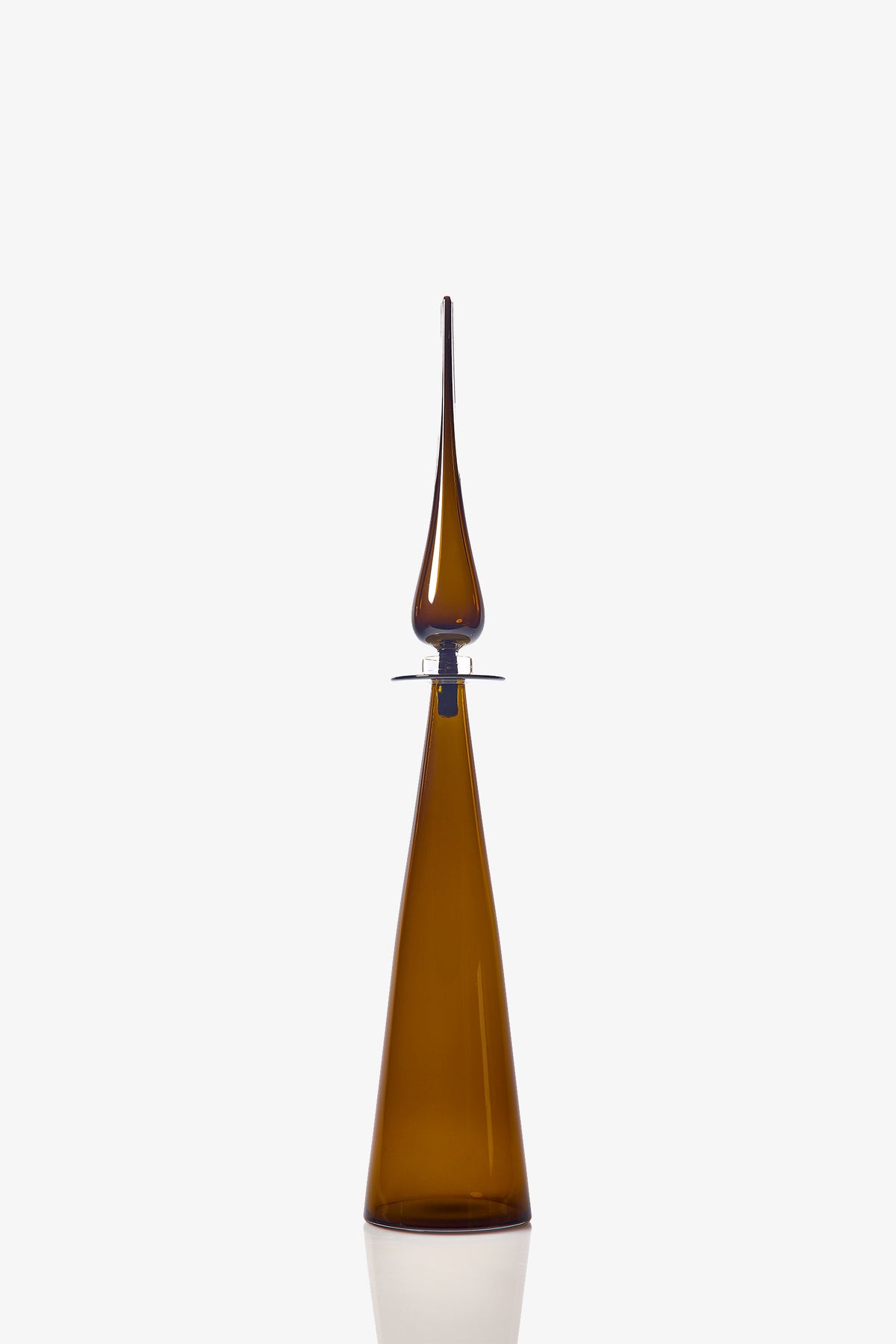 The Petite Straight Cone Decanter is a tall, slender brown glass bottle with a long, pointed stopper and a modern, minimalist design. Its reflective surface stands out against the plain white background.