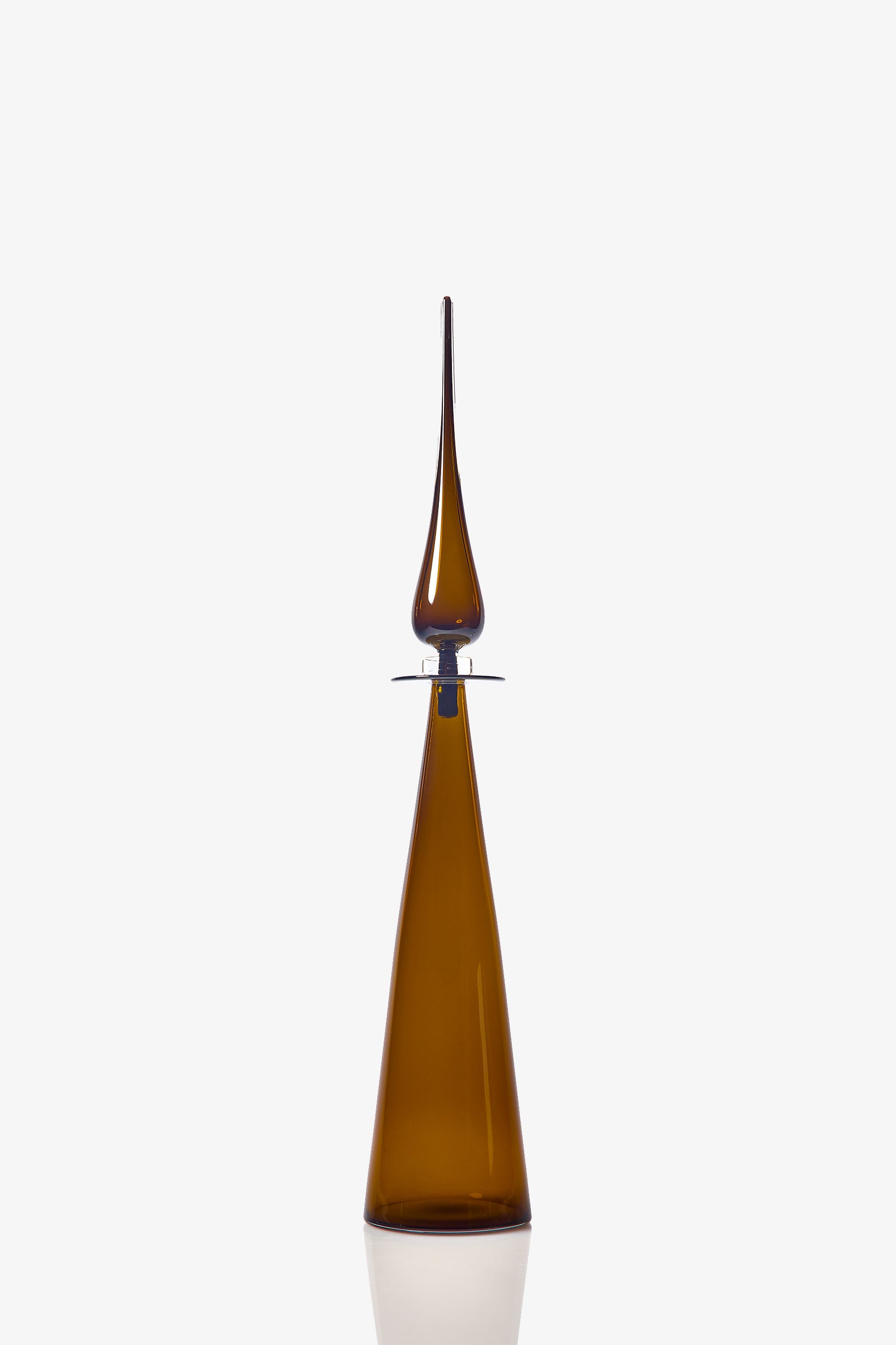 The Petite Straight Cone Decanter is a tall, slender brown glass bottle with a long, pointed stopper and a modern, minimalist design. Its reflective surface stands out against the plain white background.