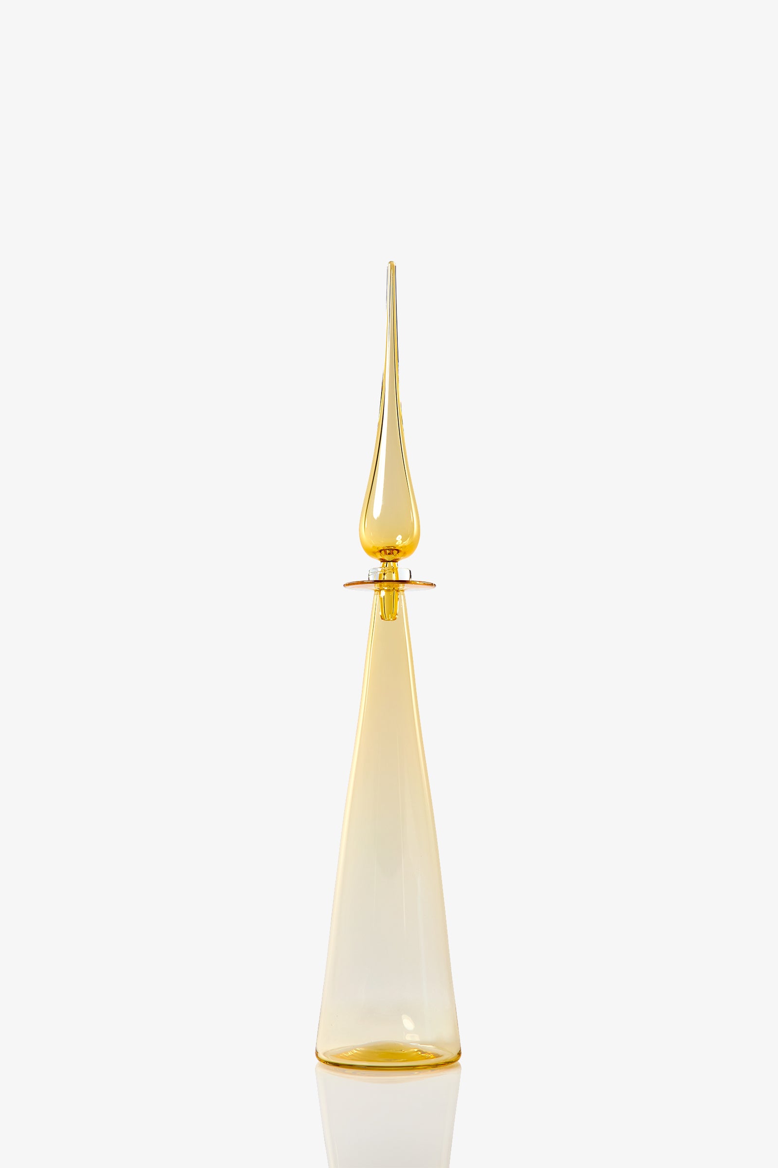 The Petite Straight Cone Decanter is a tall, elegant glass bottle with a pointed stopper in translucent amber-yellow, set against a plain white background.