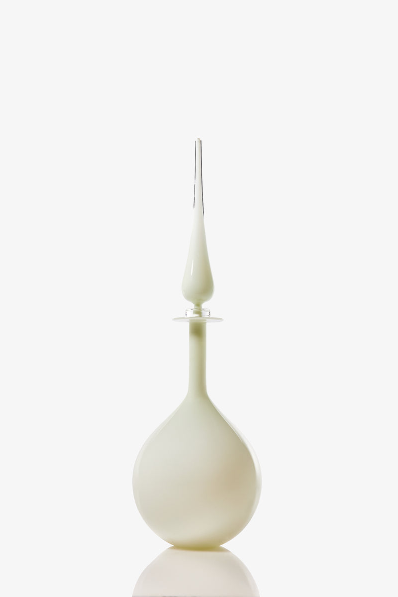 The Petite Tear Drop Decanter features a white, elegant glass bottle with a round base and a long, slender clear glass stopper, displayed against a plain white background.