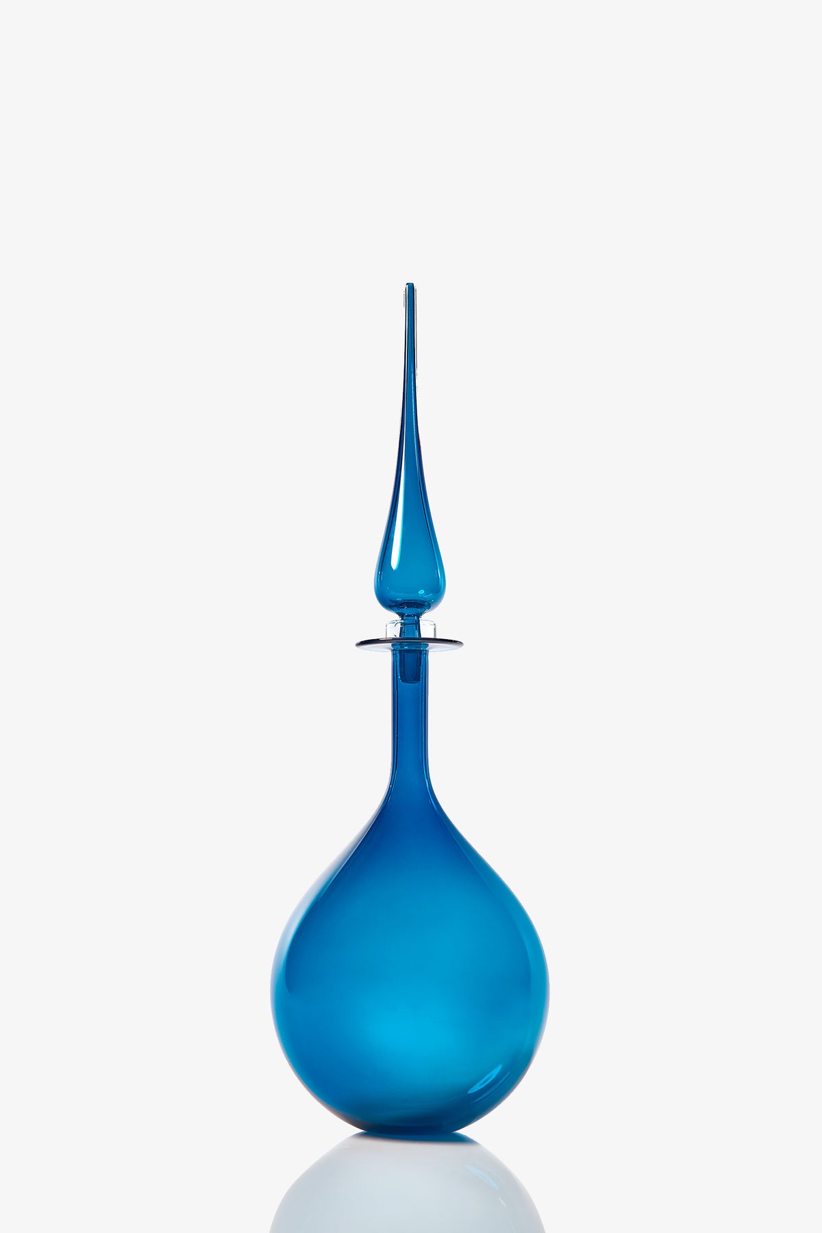 The Petite Tear Drop Decanter is a blue glass bottle with a round base and a tall, slender, pointed stopper, displayed against a plain white background.