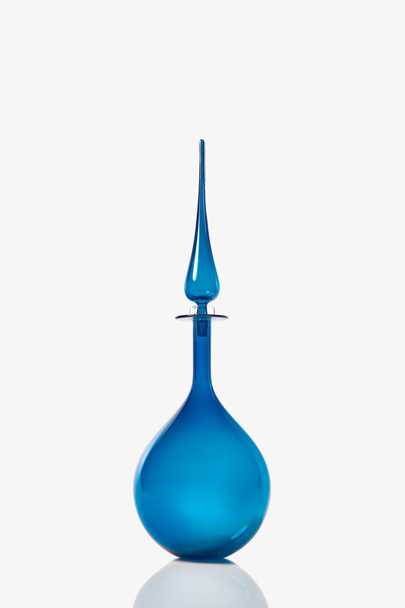 The Petite Tear Drop Decanter is a blue glass bottle with a round base and a tall, slender, pointed stopper, displayed against a plain white background.