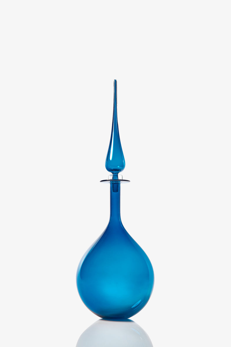 The Petite Tear Drop Decanter is a blue glass bottle with a round base and a tall, slender, pointed stopper, displayed against a plain white background.