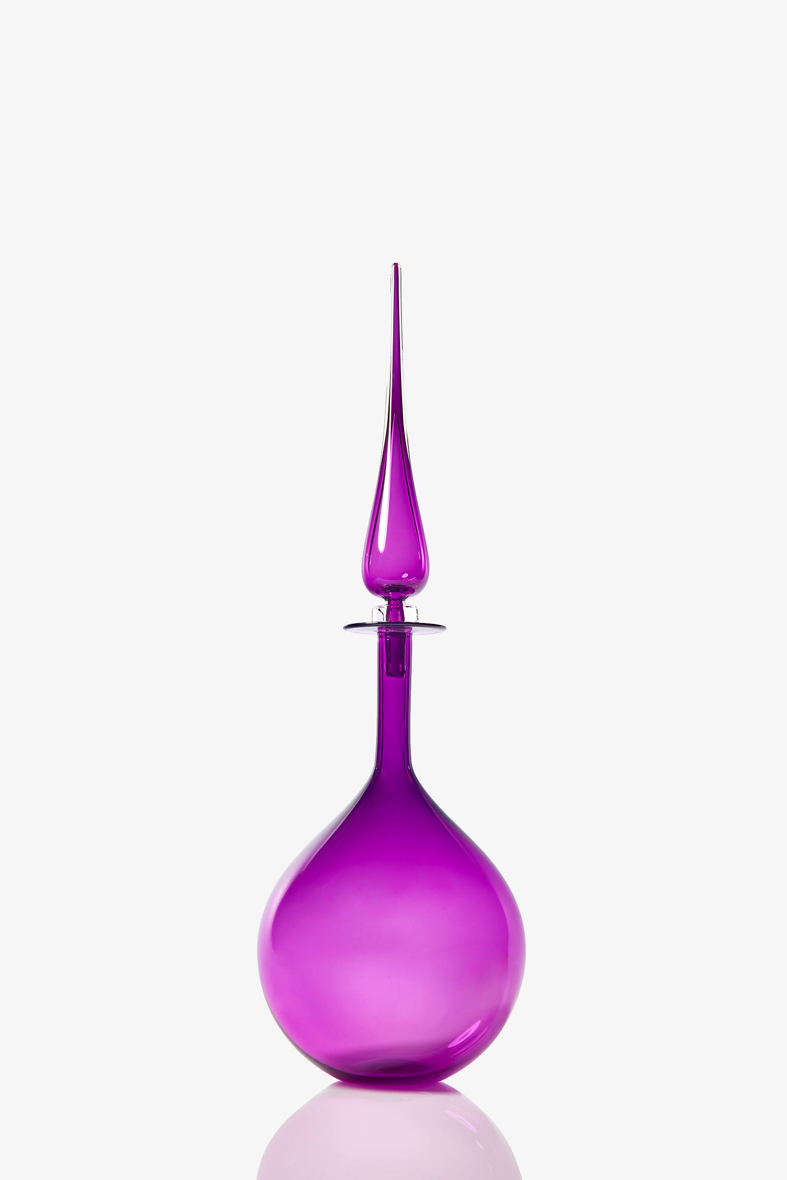 The Petite Tear Drop Decanter is a tall, elegant glass bottle with a bright purple hue, a round base, and a long pointed stopper, shown against a plain white background.