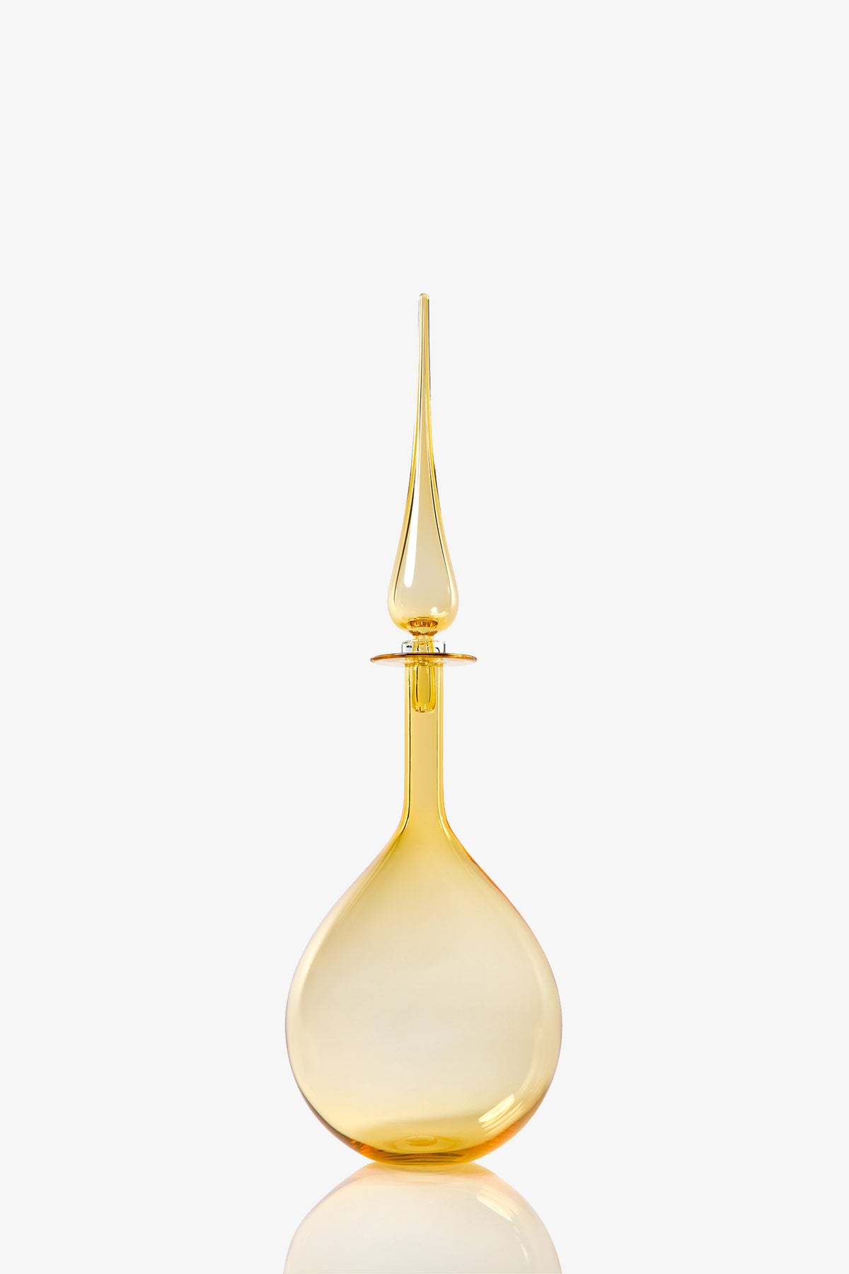 The Petite Tear Drop Decanter, made from transparent golden yellow glass, features a tall teardrop-shaped body and a long pointed stopper, displayed against a plain white background.