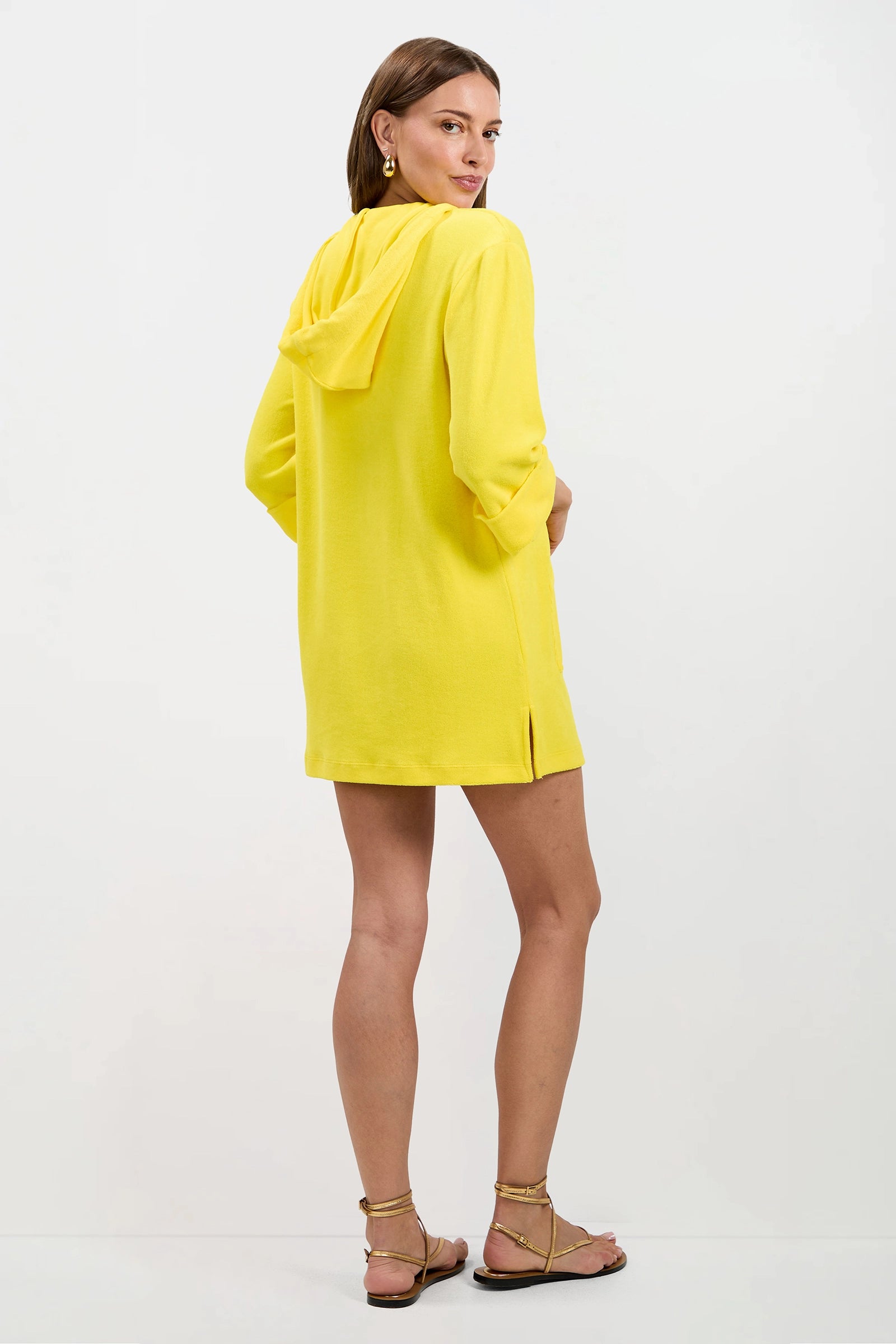 A woman with short hair, gold hoop earrings, and gold flat sandals faces away, modeling the bright yellow Poolside 3/4-Sleeve Hoodie - Poolside Terry against a plain white background.