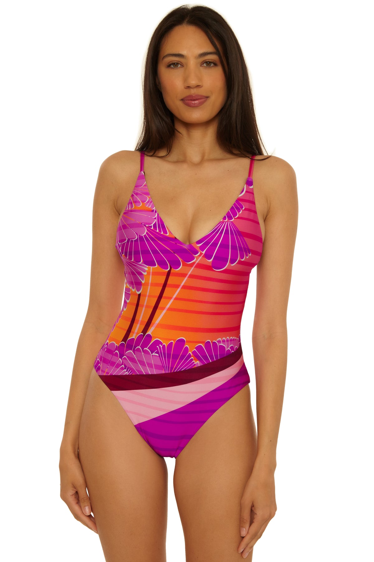 A woman wears the Rhodes V Neck Maillot, a vibrant one-piece swimsuit with pink, orange, and purple floral and striped designs, standing forward against a plain white background.