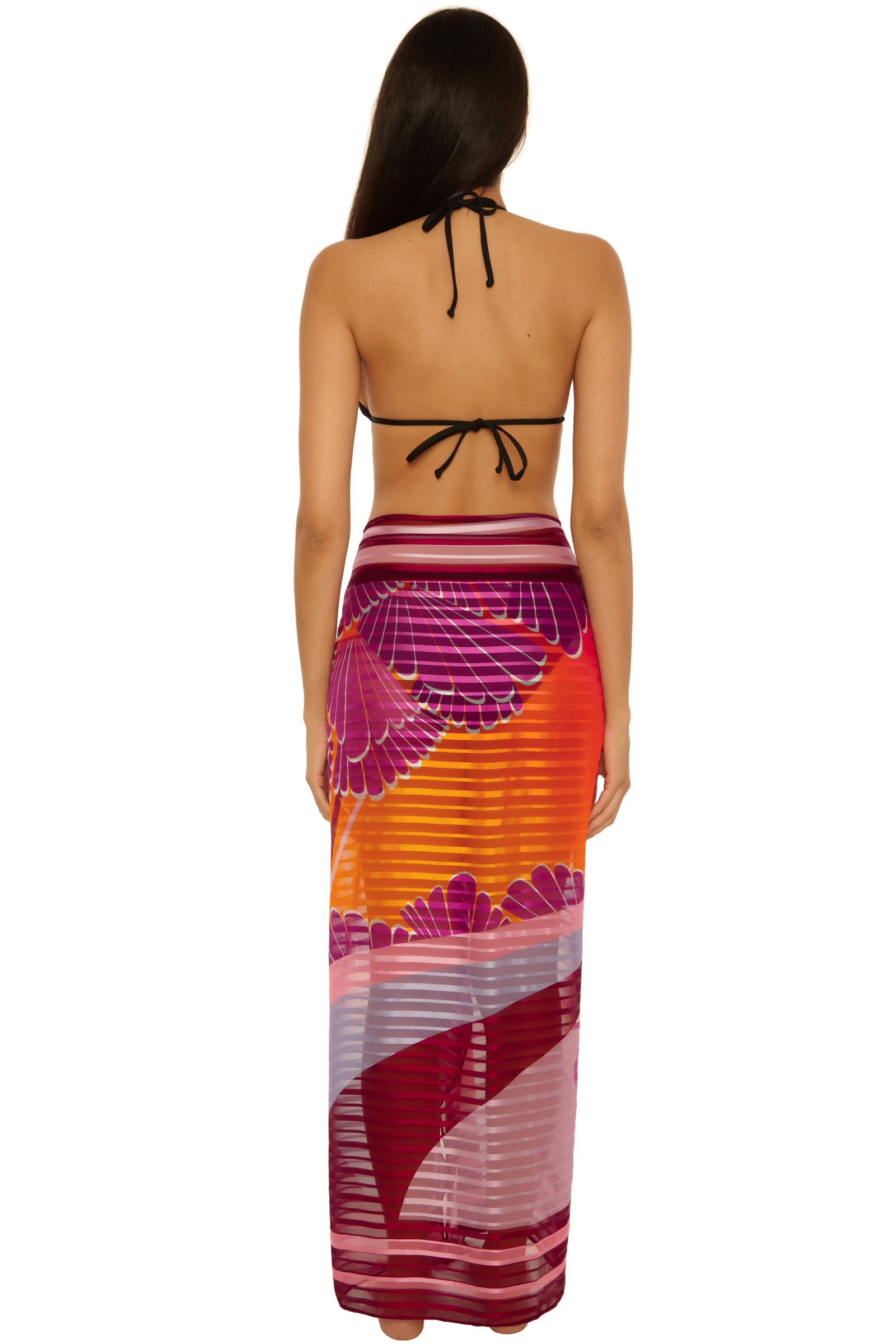 A woman with long brown hair is shown from the back wearing a black halter bikini top and the Rhodes Pareo, a long, sheer sarong featuring vibrant purple and orange patterns.