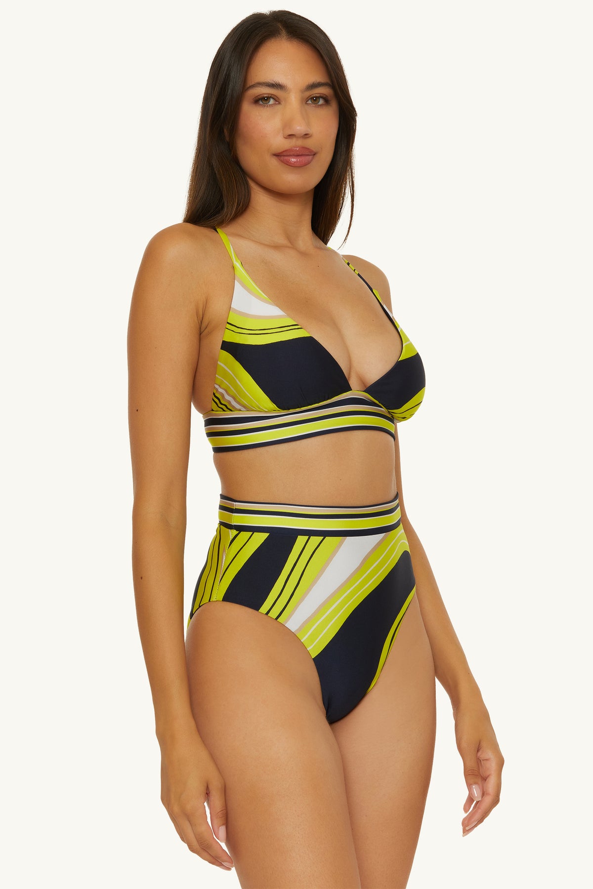 Woman wears the Reversible High-Waist Swim Bottom - Serena Swirl, a striped bikini in yellow, black, and white with a diagonal pattern, high-waisted bottom, and bralette-style top. She poses against a light background with long dark hair.