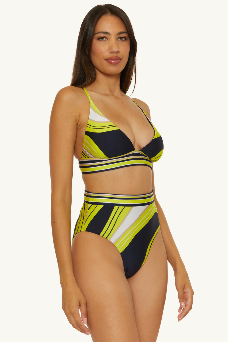 Woman wears the Reversible High-Waist Swim Bottom - Serena Swirl, a striped bikini in yellow, black, and white with a diagonal pattern, high-waisted bottom, and bralette-style top. She poses against a light background with long dark hair.