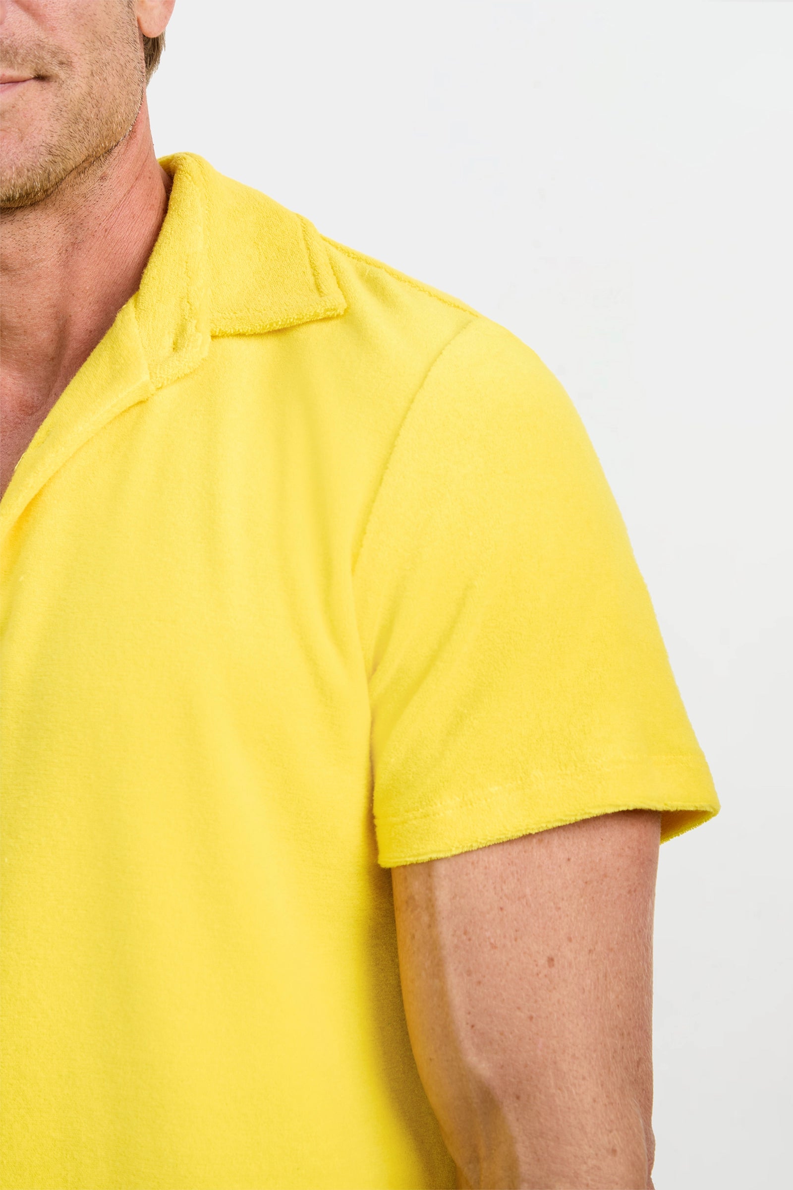 A close-up of a person wearing the Dallas Short-Sleeve Polo Shirt - Linsk Terry, featuring a bright yellow color and collar, shown from shoulders up against a white background with only the left half visible.