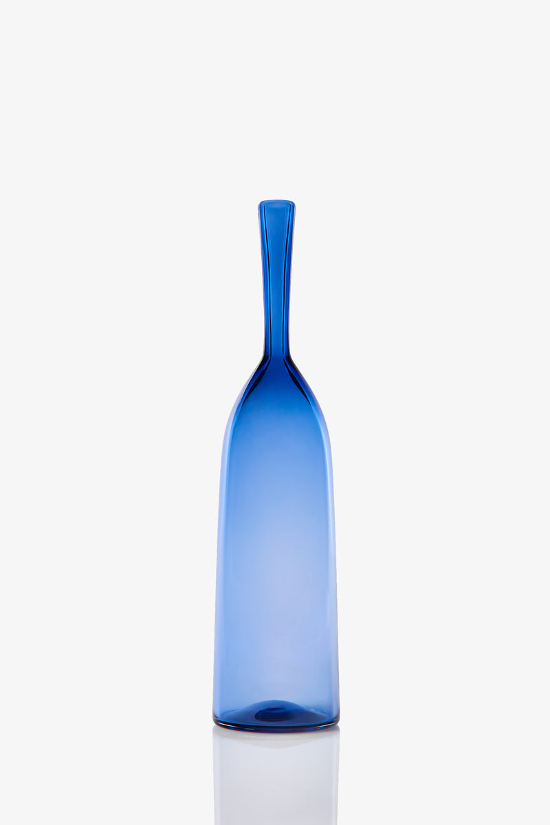 The Small Angelic Bottle is a tall, slender blue glass bottle with a narrow neck and smooth surface, shown upright against a plain white background.