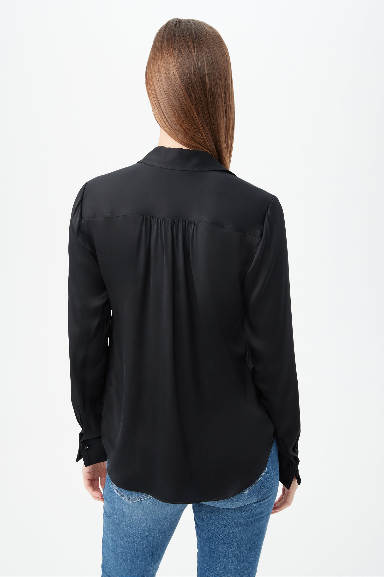 A person with straight brown hair, wearing the Cassavetes Long-Sleeve Stretch Silk Button-Up Shirt in black and blue jeans, stands with their back to the camera against a plain white background.