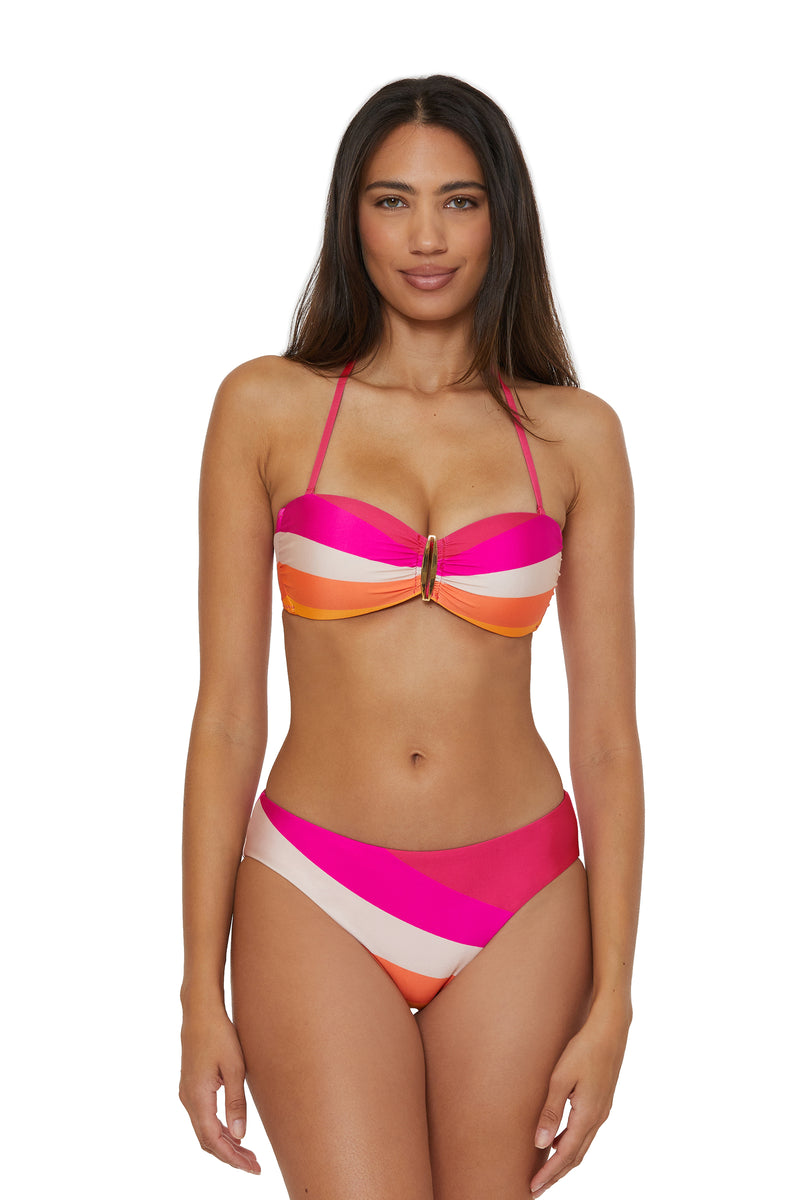 A woman with long, straight dark hair and a neutral expression wears the Hipster Swim Bottom - Sunburst, featuring colorful pink, orange, and white diagonal stripes and a gold accent at the center of the bandeau top.