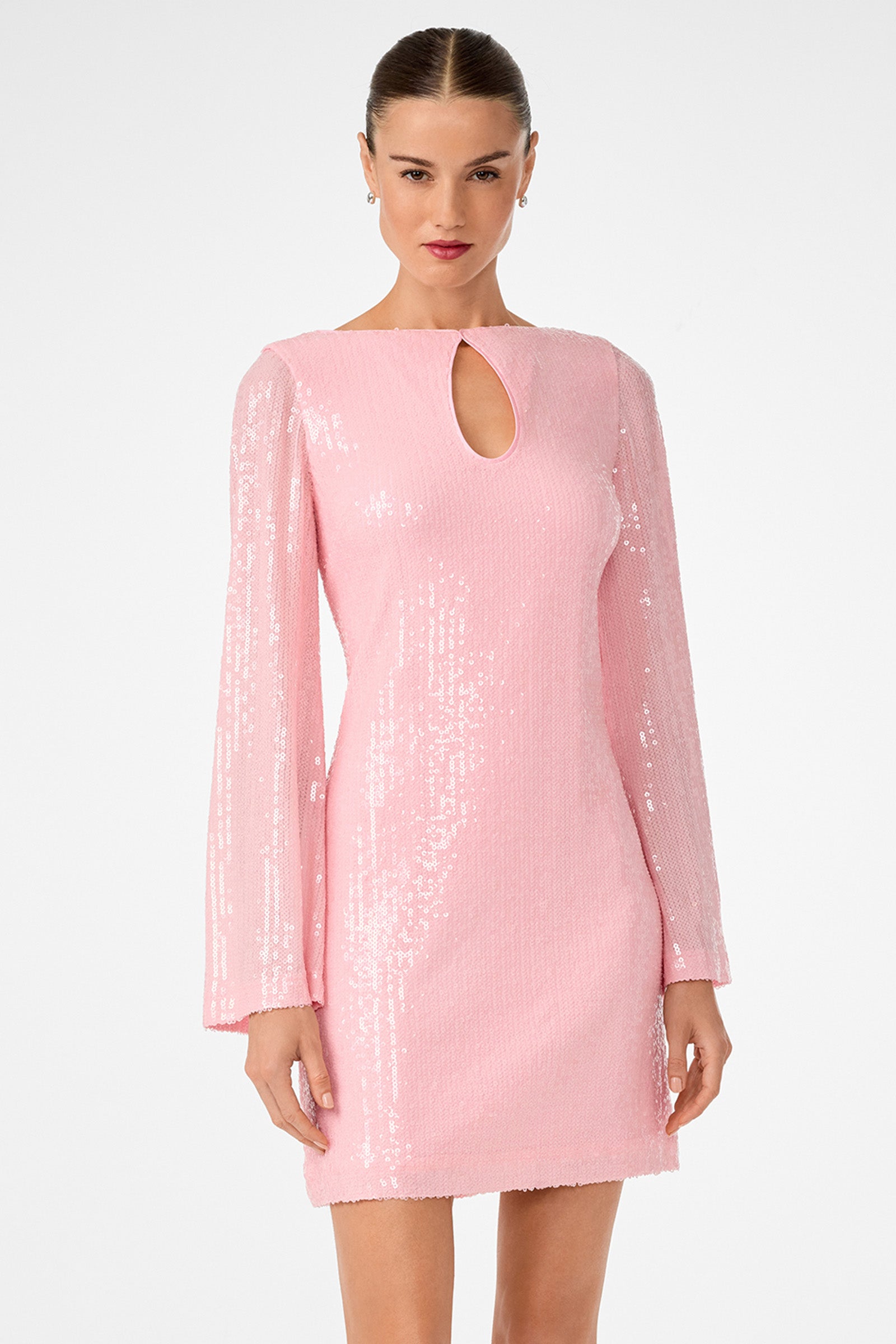 A woman wears the Singles 2 Dress, a light pink sequined mini with long sleeves and a small teardrop keyhole at the neckline, standing against a plain white background.