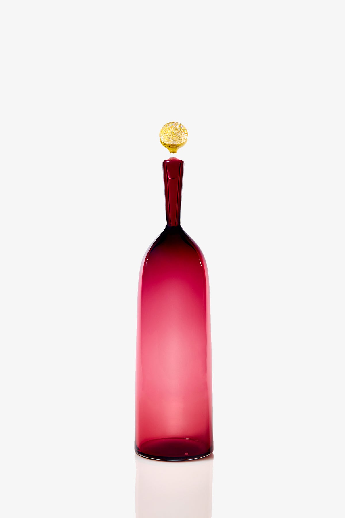 The Tall Bottle Carmella Barware features a deep pink, slender glass body with a long neck and a rounded yellow textured stopper, displayed against a plain white background.