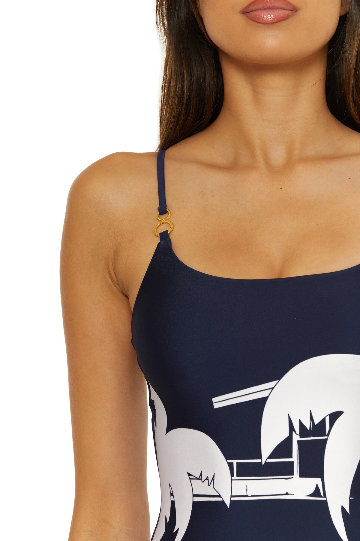 A woman wears the Scoop Neck One-Piece Swimsuit - Trina Tennis, featuring a navy blue base with white abstract palm tree and building prints, thin straps, and a gold ring detail on one shoulder. Shown from shoulders to mid-torso.
