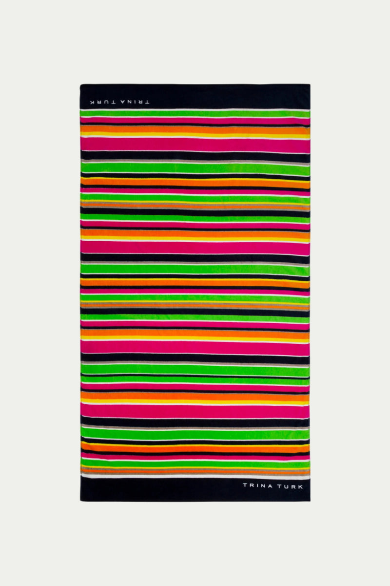The TT Anniversary Stripe Terry Cloth Towel features multi-colored horizontal stripes in bright shades, black borders, and TRINA TURK in white on opposite edges.