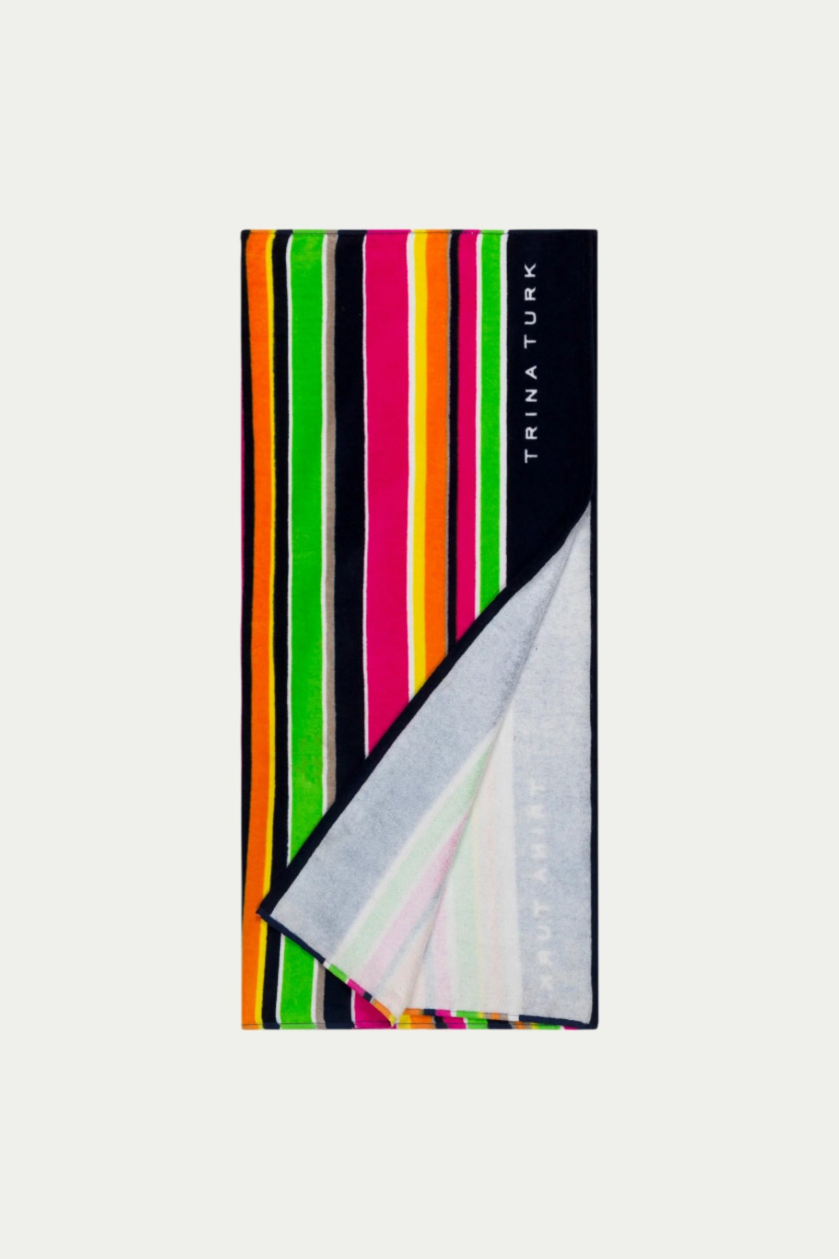 The TT Anniversary Stripe Terry Cloth Towel features bold vertical stripes in green, orange, pink, yellow, and black with a white underside. The black edge is printed with TRINA TURK in white.
