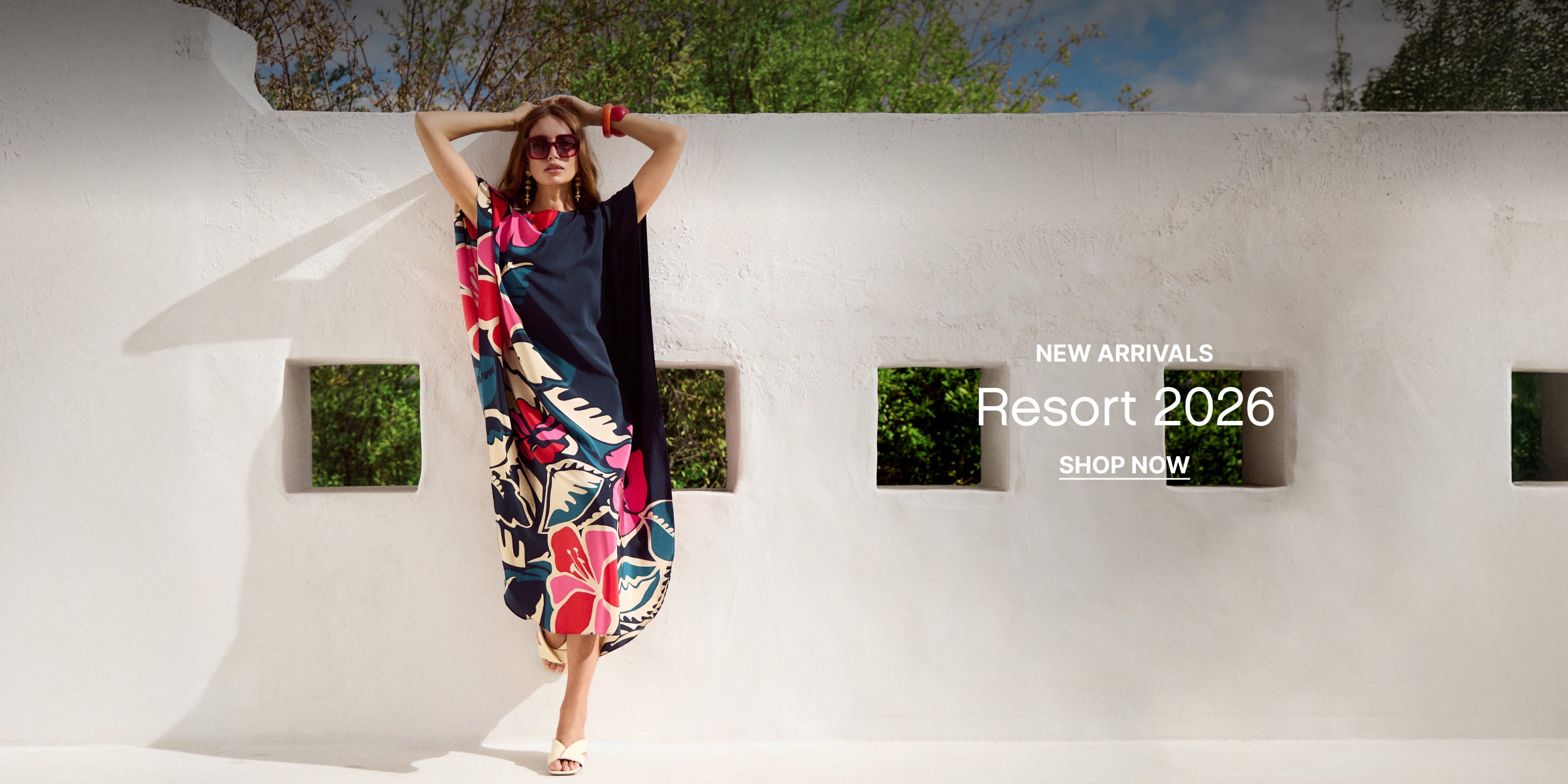 Woman in a colorful dress standing against a white wall with 'New Arrivals Resort 2026' text.
