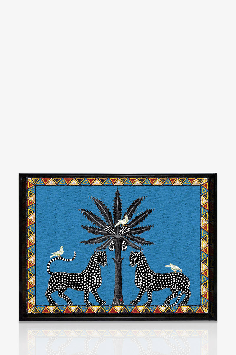 The Ortigia Large Tray displays two black-spotted leopards facing a central palm tree with white birds perched nearby, set against a blue background and bordered by vibrant geometric patterns.