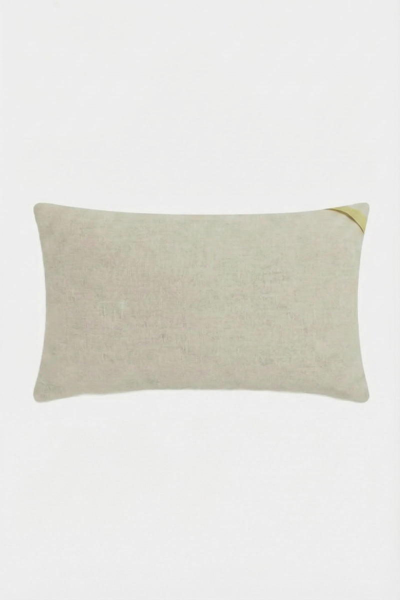 The Amazing Maze Embroidered Pillow is a rectangular, light beige cushion with a subtle texture and a small golden ribbon on one corner, displayed against a white background.