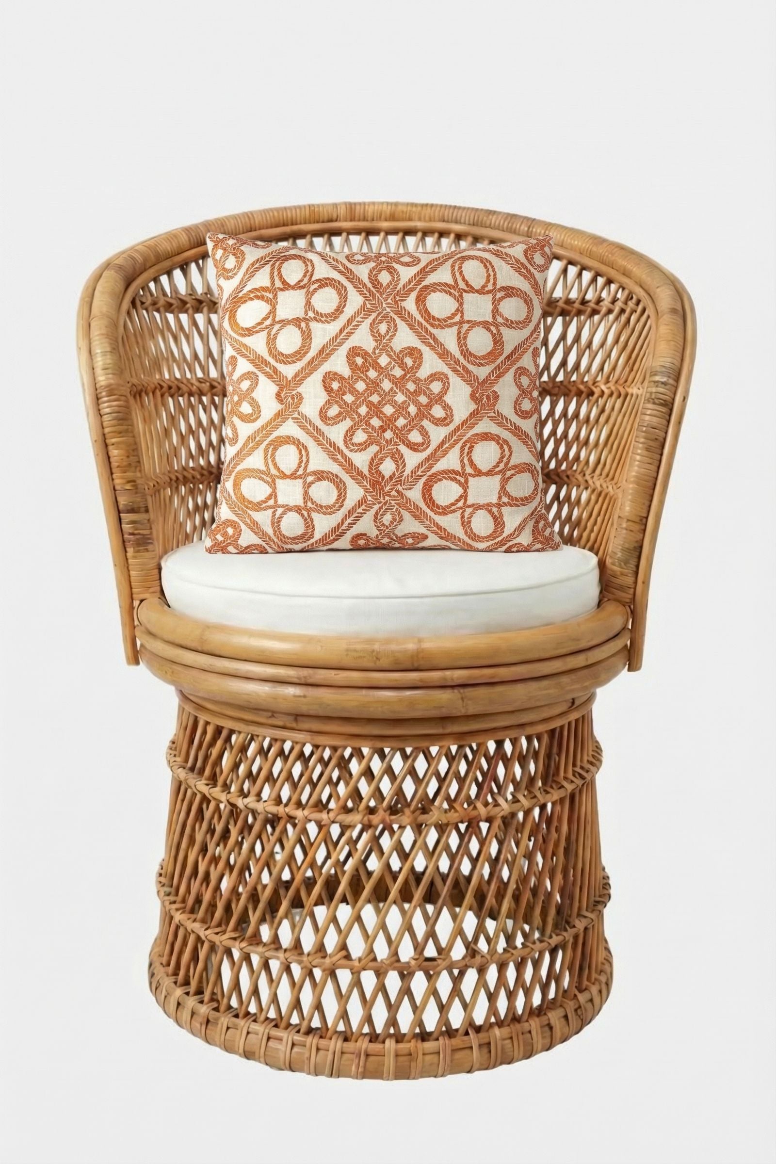 A round wicker chair with an open-weave design, white seat cushion, and the Costa Mesa Embroidered Square Pillow featuring an orange geometric pattern on a white background, set against a plain white backdrop.