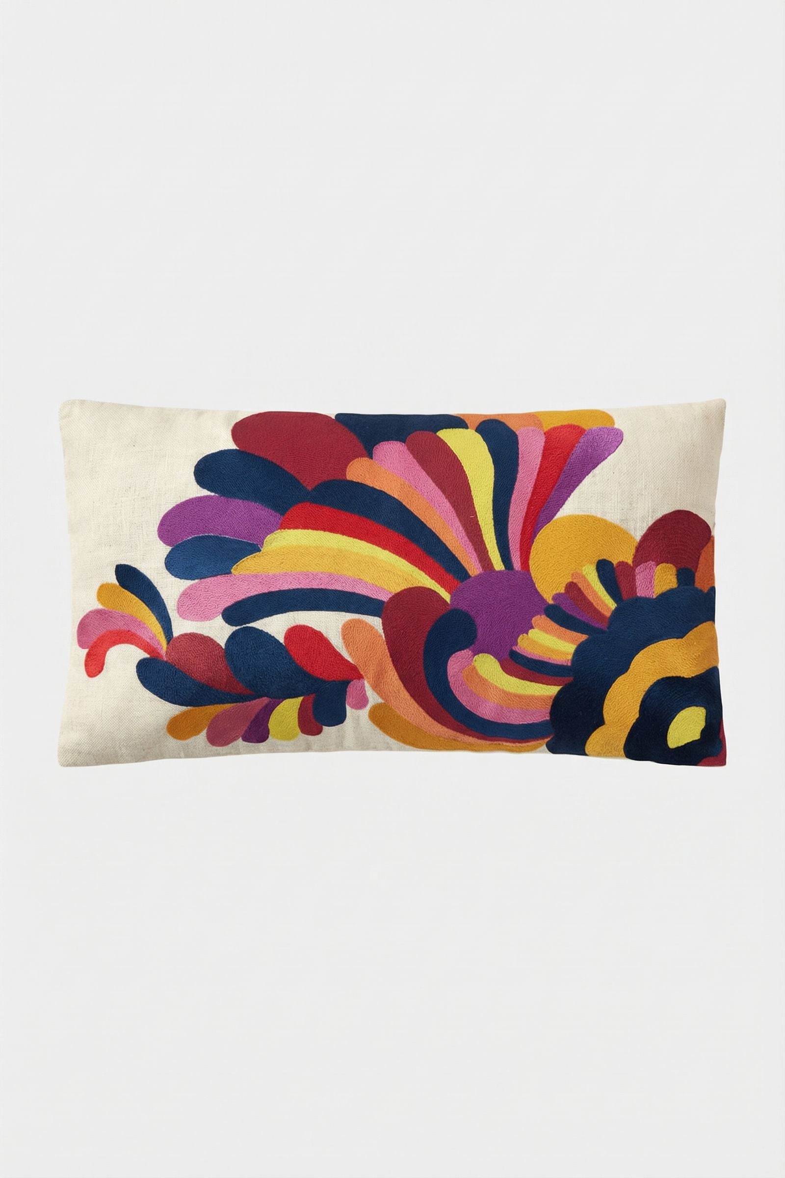 The Escondido Embroidered Lumbar Pillow features a cream background and a vibrant, abstract design in red, yellow, pink, blue, orange, and purple that evokes stylized floral or feather shapes.