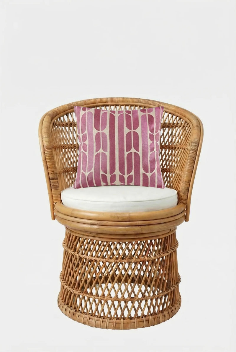 A rattan chair with a round white cushion and the Palmdale Emb Pillow 20X20", which has a pink and white geometric pattern, set against a plain white background.