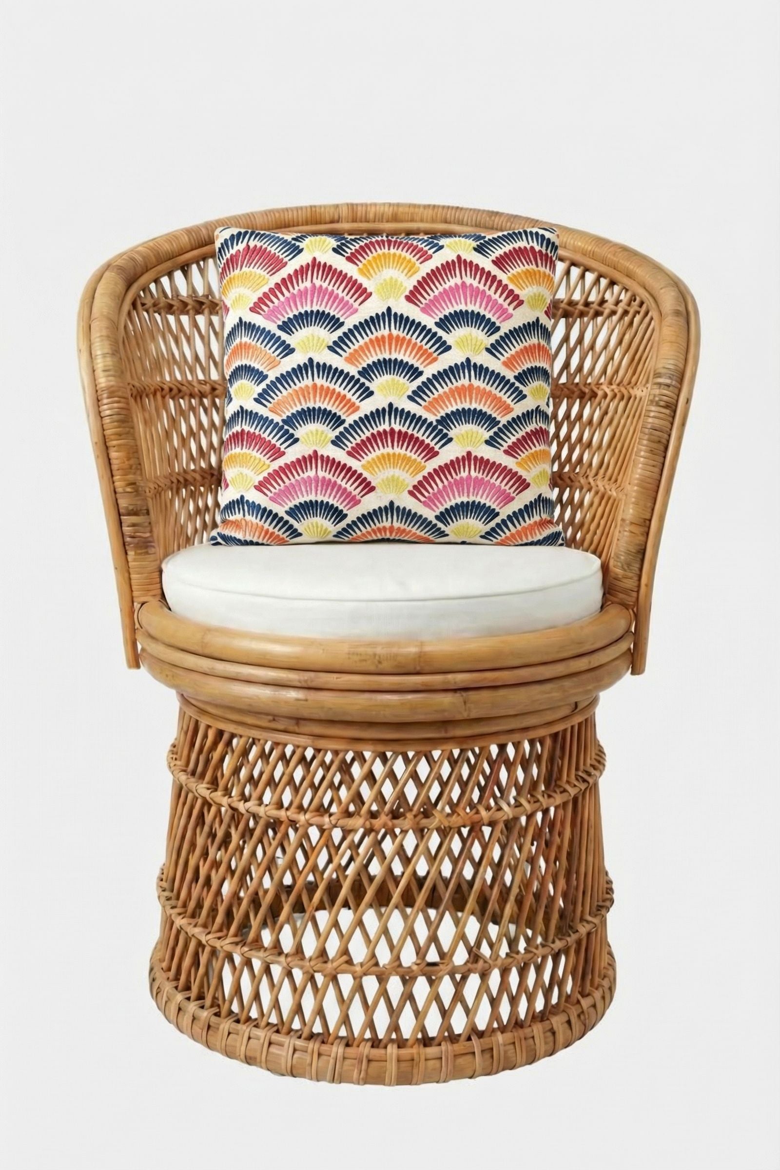 A round rattan chair with a white cushion and the Pasadena Embroidered Throw Pillow, featuring a geometric fan pattern in red, blue, yellow, and white, set against a plain white background.