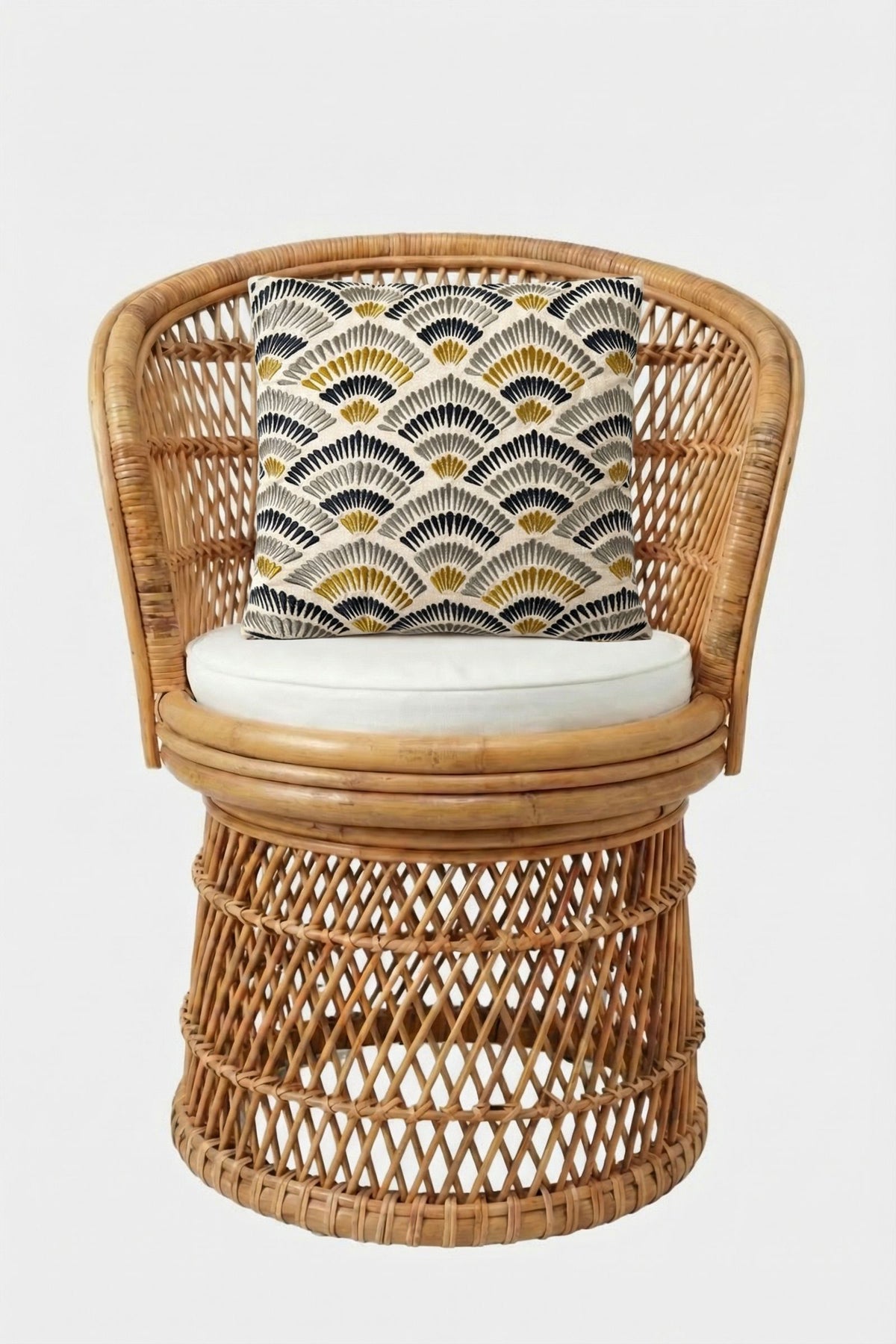A round rattan chair with an intricate woven pattern and a white seat cushion, styled with the Pasadena Embroidered Square Pillow, which features a geometric fan-like design in black, white, and yellow. The background is plain white.