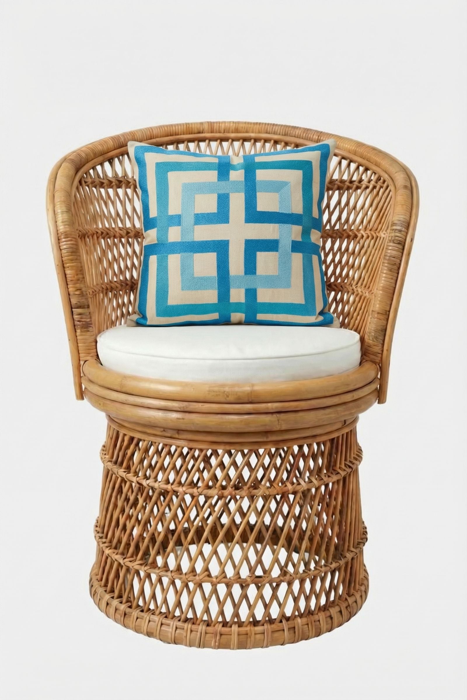 A round rattan chair with a woven design features a white seat cushion and the Shanghai Links Embroidered Throw Pillow, which has a blue geometric pattern on beige. The chair is set against a plain white backdrop.