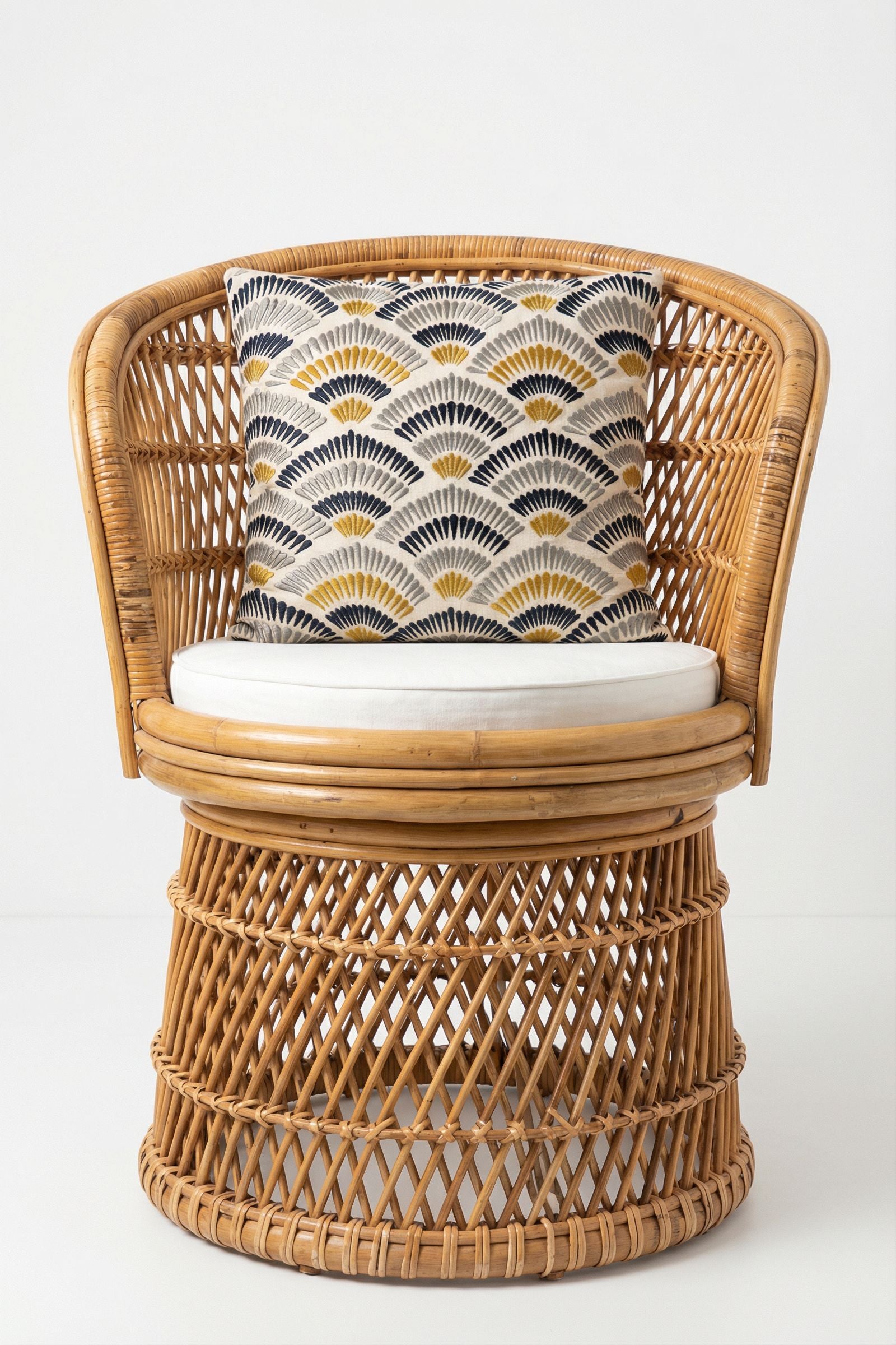 A round rattan chair with a white cushion and the Pasadena Embroidered Throw Pillow, which showcases a fan-shaped geometric design in black, yellow, and white, is displayed against a plain white background.