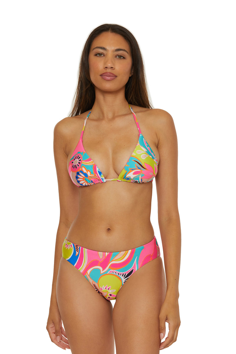 A woman with long brown hair models the Reversible Hipster Swim Bottom - Venus, featuring a colorful, floral pattern and high-cut style. She faces the camera against a plain white background.