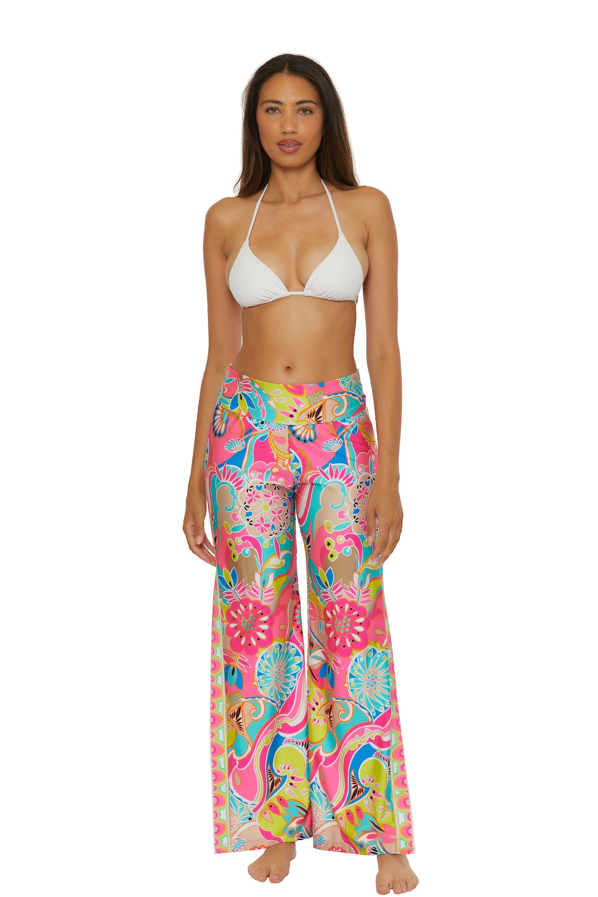 A woman stands barefoot, facing forward against a white background, wearing a white bikini top and Venus Swim Cover-Up Pant in colorful floral and abstract patterns.