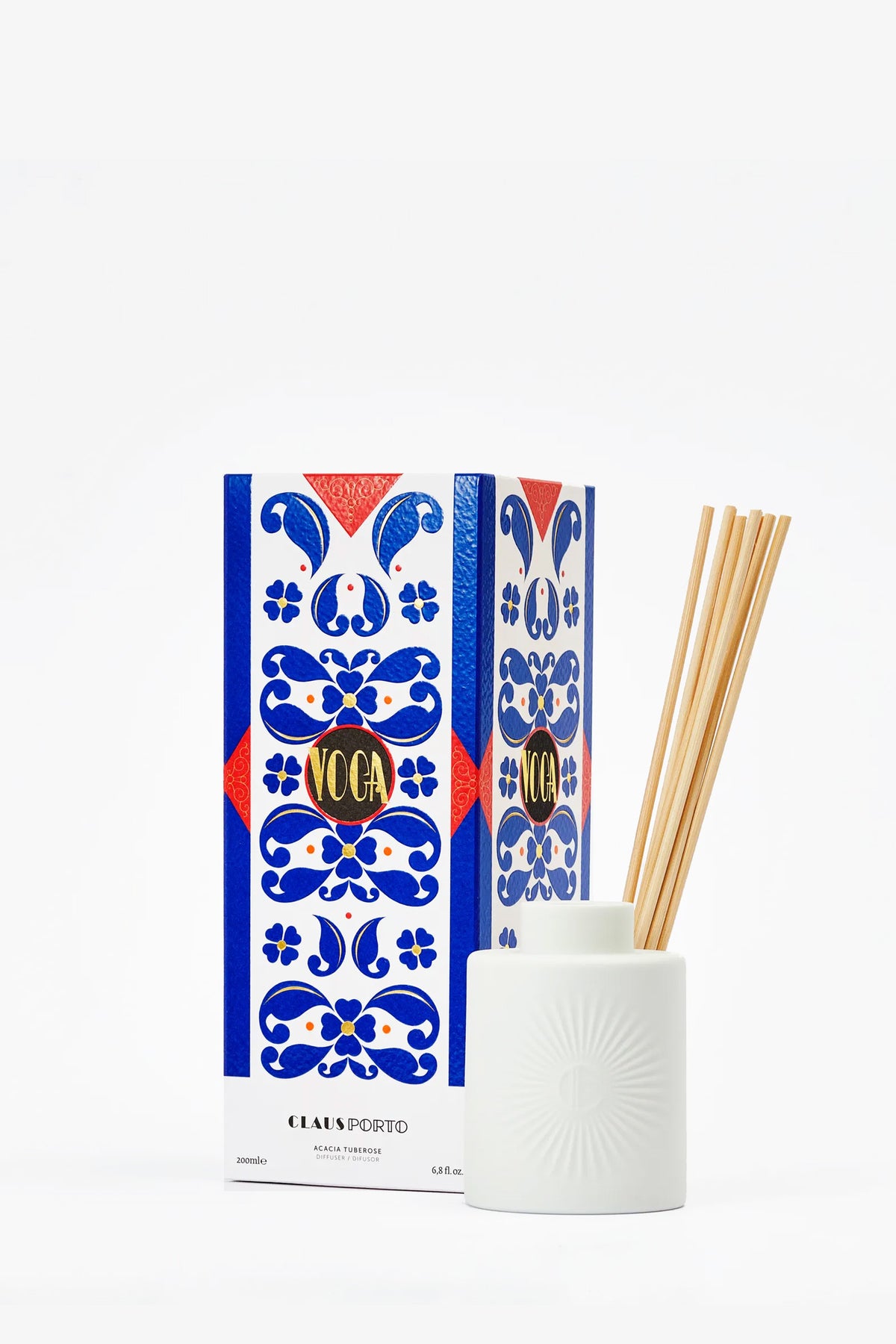 A Claus Porto Voga Diffuser featuring a white ceramic holder with upright wooden reeds, presented in a blue and white patterned box.