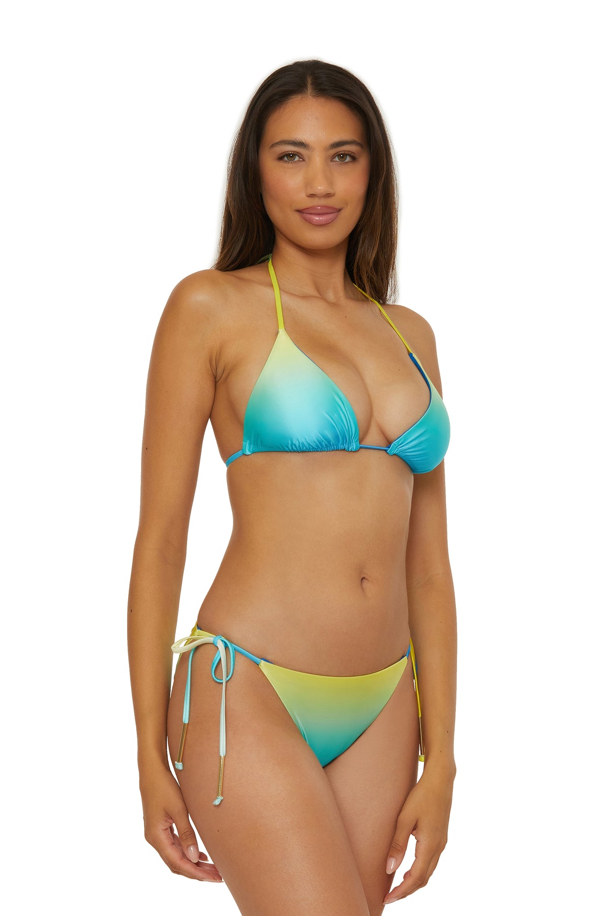 A woman with long brown hair wears the Reversible Tie Side Swim Bottom - West Palm, featuring side-tie bottoms and a blue-yellow gradient, as she stands against a white background, looking at the camera with a slight smile.