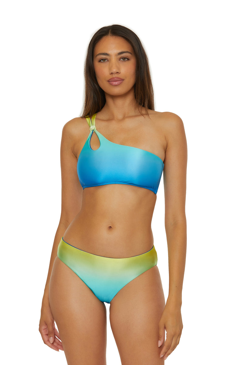A woman with long straight hair and a neutral expression faces forward, wearing the One Shoulder Swim Top - West Palm in a blue and green ombre design featuring a one-shoulder silhouette with a keyhole cutout near the strap.