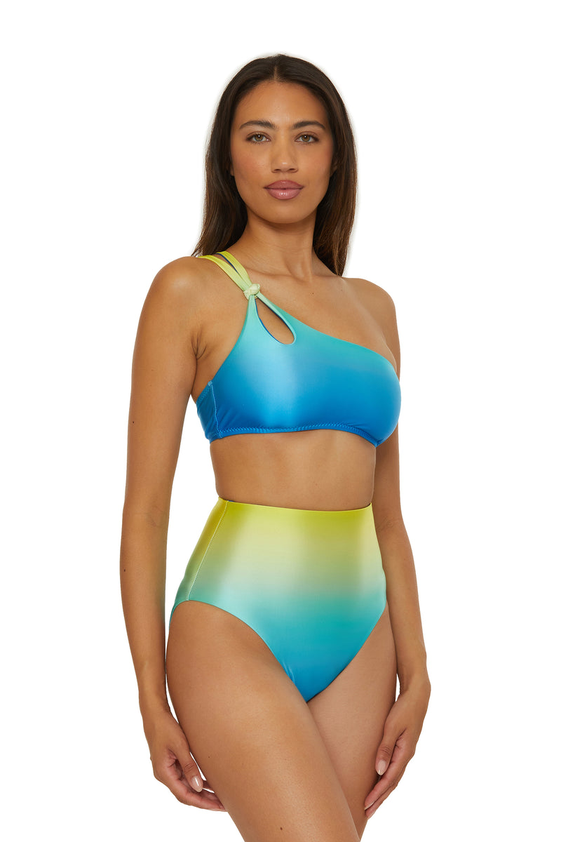 A woman wears the One Shoulder Swim Top - West Palm, featuring a blue-to-green gradient and cutout by the strap, standing against a white background.