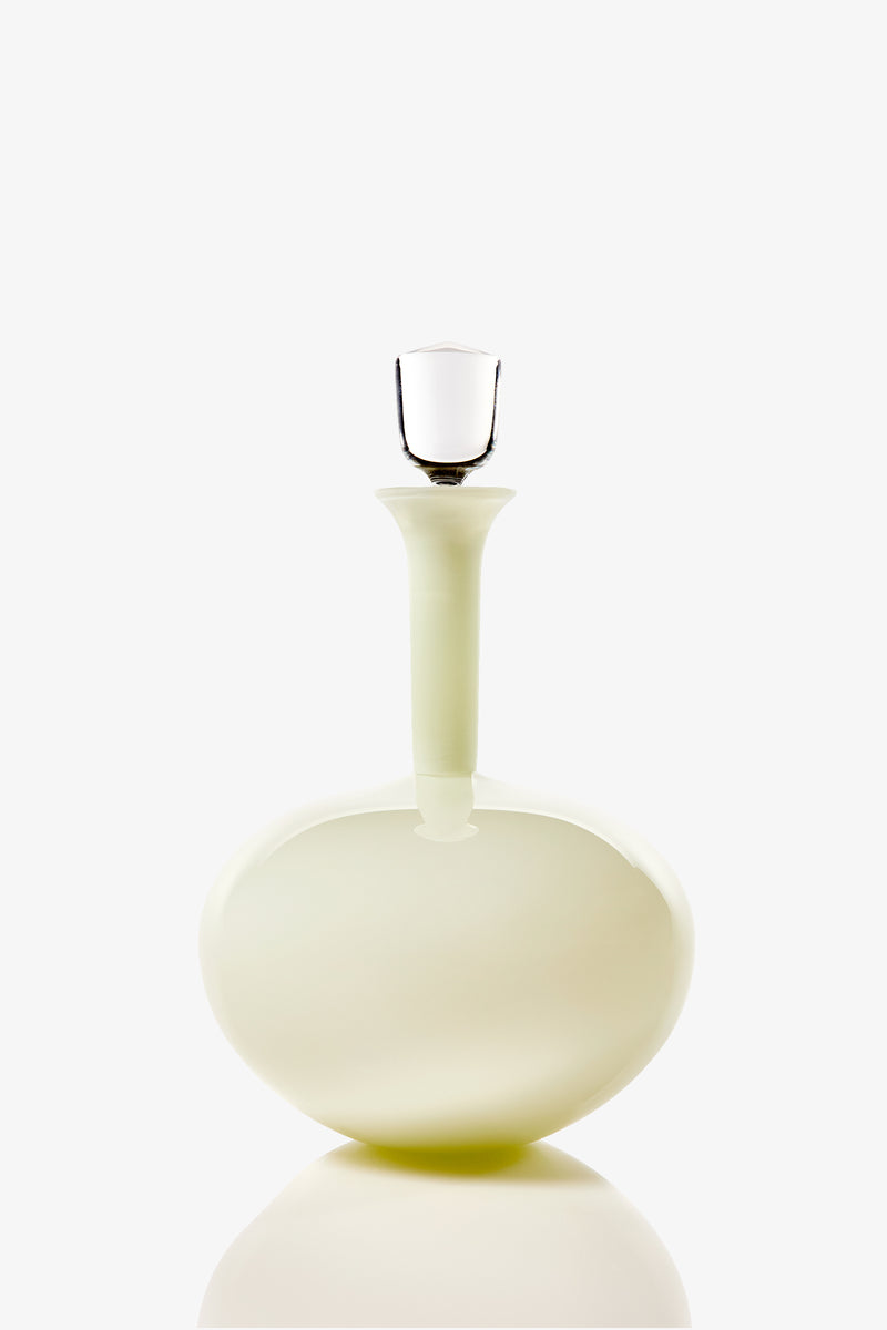 The Wexler Low Oval Bottle is a round, pale glass decanter featuring a long neck and a clear glass stopper, shown against a plain white background.