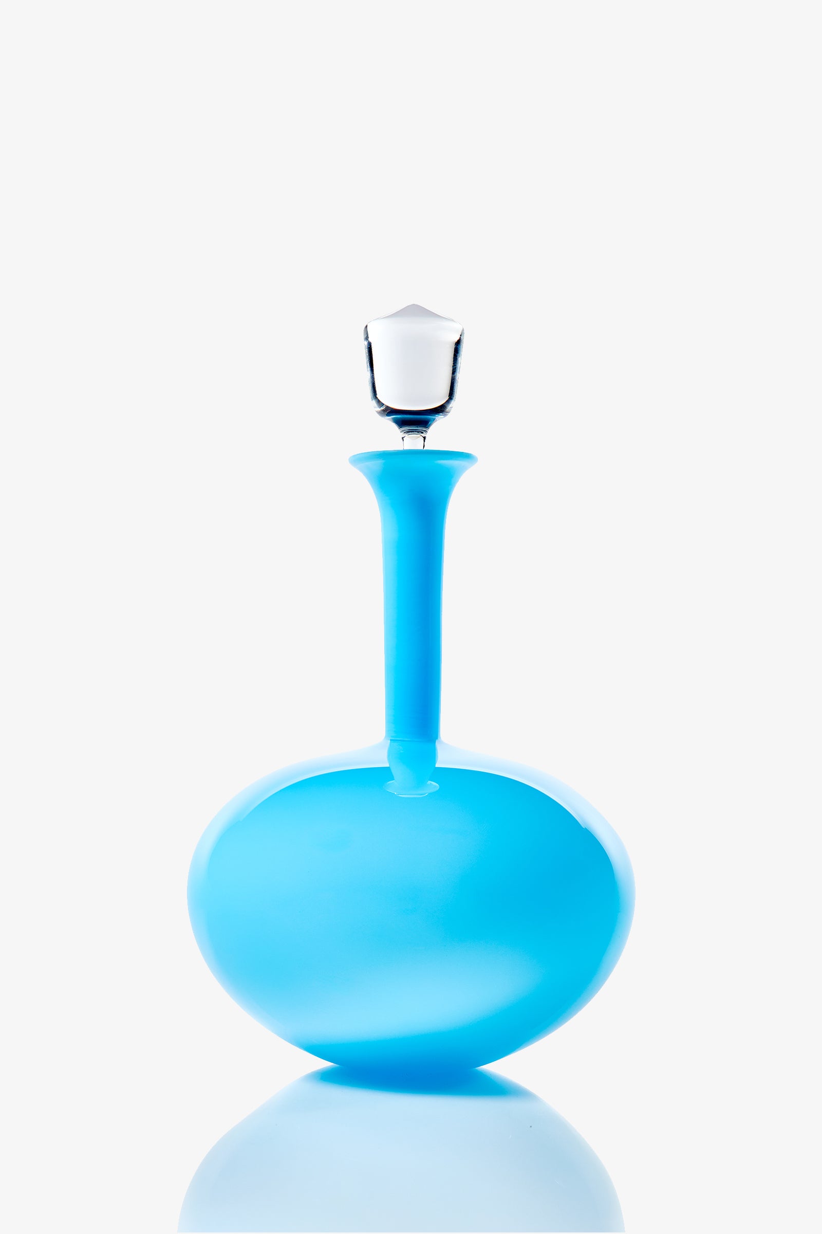 The Wexler Low Oval Bottle is a modern, round blue glass decanter featuring a long neck and a clear glass stopper, shown against a white background with a subtle reflection below.