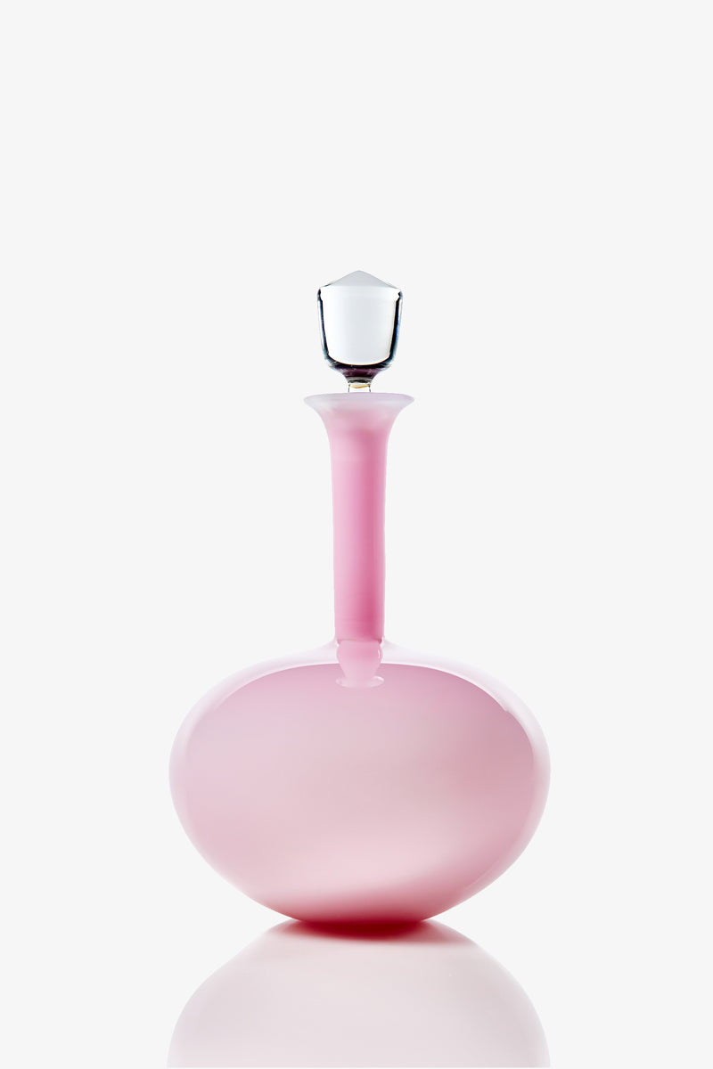 A Wexler Low Oval Bottle in pink glass, featuring a rounded base, a long narrow neck, and a clear faceted stopper, photographed against a white background.