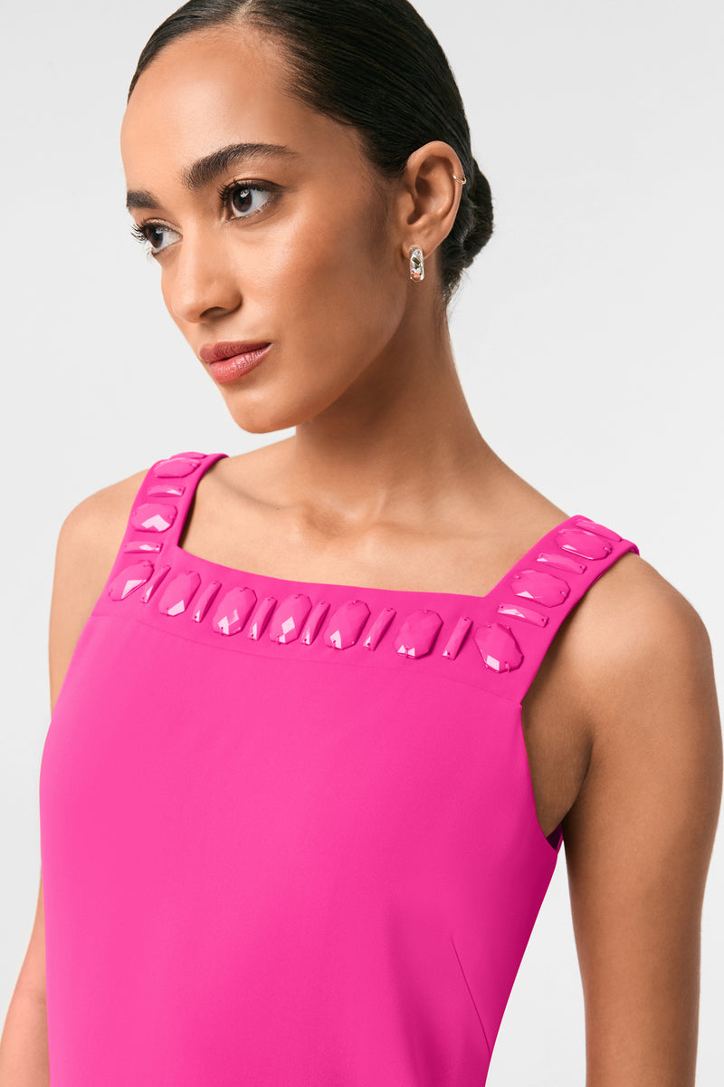 A woman in the Yokuna Jewel Neck Mini Dress, a bright pink sleeveless style with glossy accents at the square neckline, wears small hoop earrings and looks slightly to the side against a plain light background.