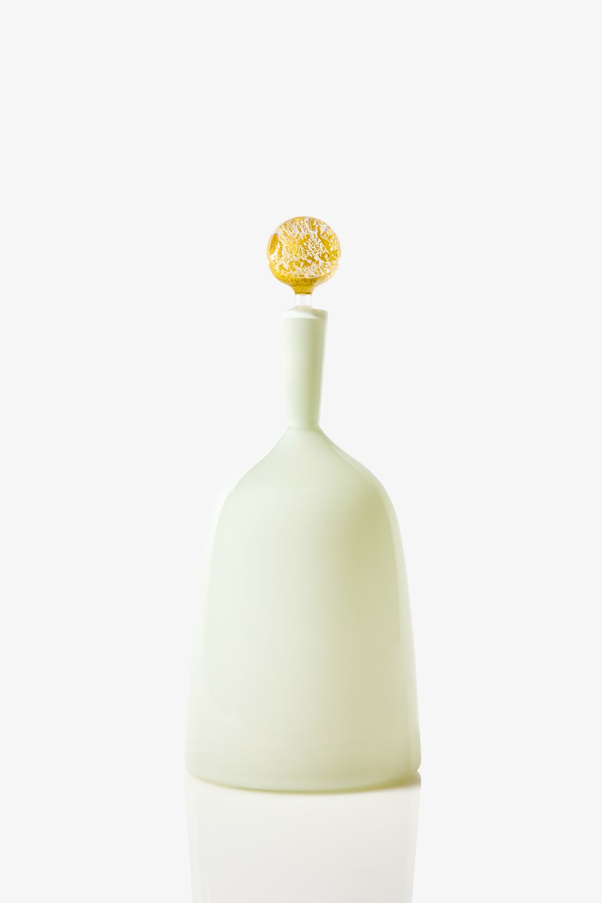 The Wide Bottle Carmella Barware features a minimalist design with frosted white glass, a tall neck, and a round, textured golden stopper, all set against a plain white background.